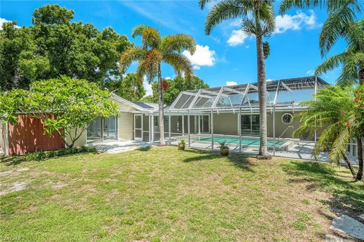 Back of house with a patio, glass enclosure, and a lawn
