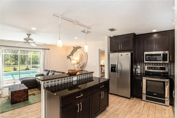 Kitchen featuring ceiling fan, stainless steel appliances, rail lighting, decorative backsplash, and dark stone countertops