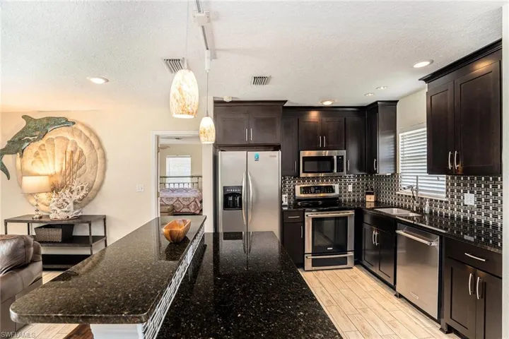 Kitchen featuring dark stone countertops, hanging light fixtures, appliances with stainless steel finishes, and a textured ceiling