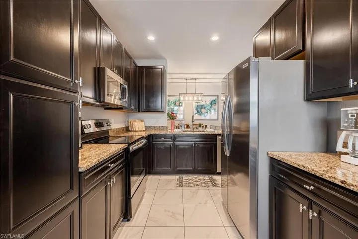 Kitchen with dark brown cabinetry, light stone countertops, marble finish floor, stainless steel appliances, and recessed lighting
