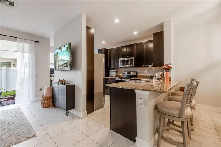 Kitchen featuring light stone counters, stainless steel appliances, visible vents, dark brown cabinetry, and a kitchen bar