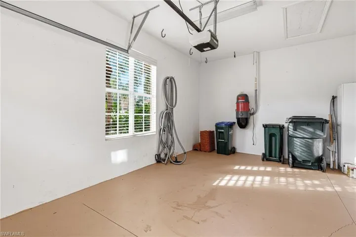 Spacious garage featuring a window with blinds, painted concrete flooring, an overhead garage door opener, and a wall-mounted central vacuum system
