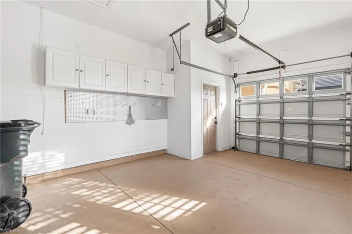 Garage space featuring an automatic overhead door, overhead storage cabinetry, pegboard organization, an interior access door, and a finished concrete floor