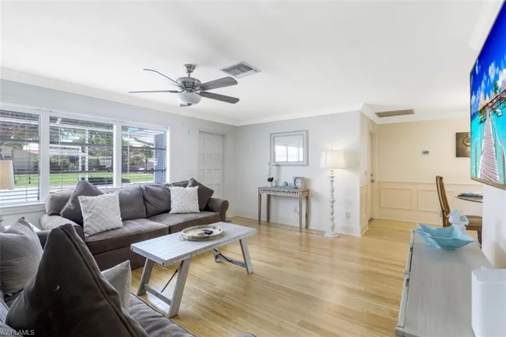 Living area featuring ornamental molding, light wood finished floors, a wainscoted wall, and ceiling fan