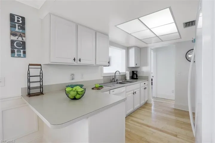 Kitchen featuring white cabinetry, a peninsula, white appliances, light countertops, and light wood finished floors