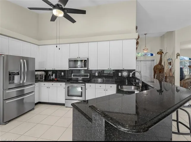 Kitchen with light tile patterned floors, a sink, appliances with stainless steel finishes, a peninsula, and backsplash