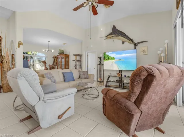 Living area with light tile patterned floors, ceiling fan with notable chandelier, and vaulted ceiling
