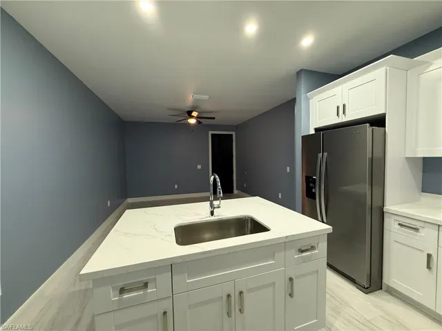 Kitchen featuring stainless steel refrigerator with ice dispenser, white cabinets, a center island with sink, light stone countertops, and ceiling fan