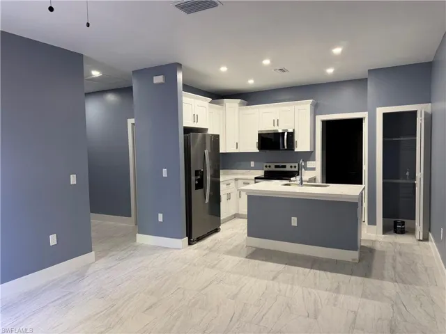 Kitchen featuring a center island with sink, stainless steel appliances, white cabinets, recessed lighting, and light stone countertops