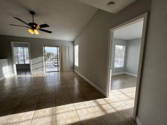 Tiled empty room with a textured ceiling, a ceiling fan, and baseboards