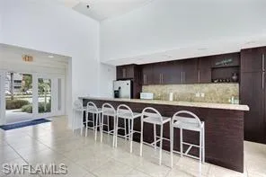 Kitchen with tasteful backsplash, freestanding refrigerator, dark brown cabinetry, light countertops, and a breakfast bar area