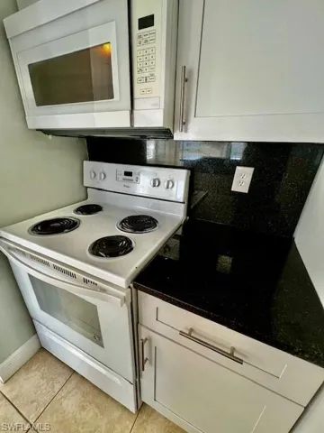 Kitchen with light tile patterned flooring, white cabinetry, white appliances, and backsplash