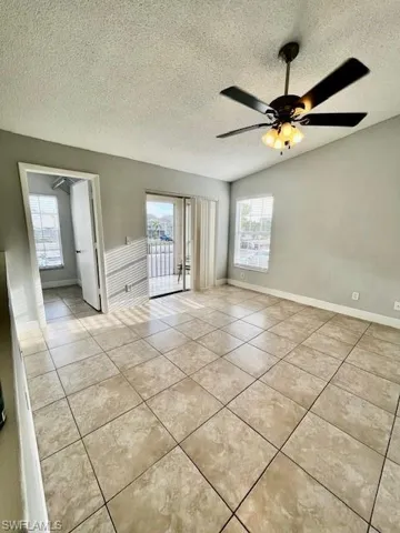 Empty room with light tile patterned flooring, a textured ceiling, ceiling fan, and baseboards