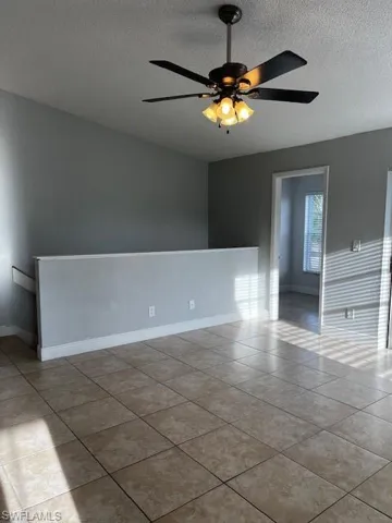 Spare room with tile patterned floors, baseboards, ceiling fan, and a textured ceiling
