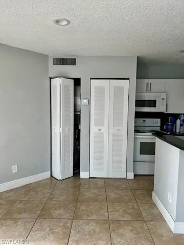 Kitchen featuring visible vents, white cabinetry, white appliances, dark countertops, and a textured ceiling