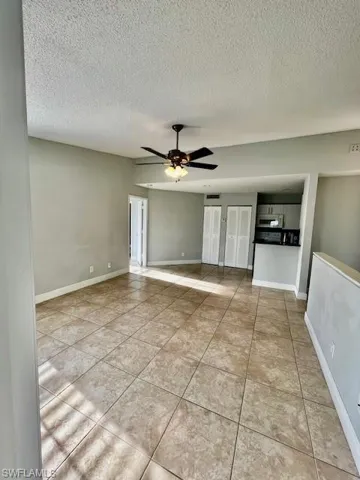 Tiled empty room with a textured ceiling, ceiling fan, and baseboards