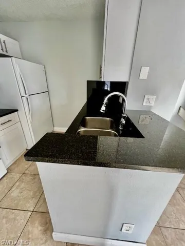 Kitchen featuring a peninsula, a sink, white cabinets, and freestanding refrigerator