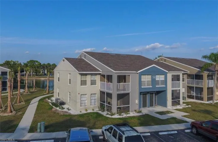 Back of property with a balcony, a yard, a water view, stucco siding, and uncovered parking