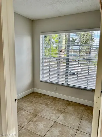 Empty room featuring light tile patterned floors, a textured ceiling, baseboards, and a healthy amount of sunlight