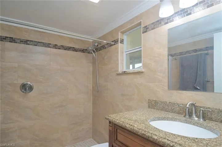 Bathroom with tasteful backsplash, ornamental molding, vanity, and tiled shower