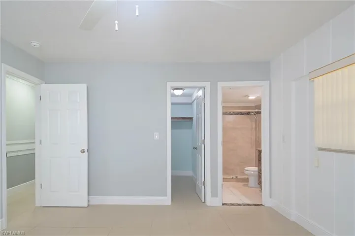 Unfurnished bedroom with ceiling fan, light tile patterned floors, a closet, a spacious closet, and ensuite bathroom