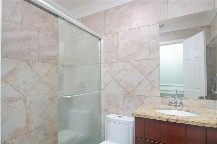 Bathroom featuring vanity, tile walls, crown molding, toilet, and a shower with door