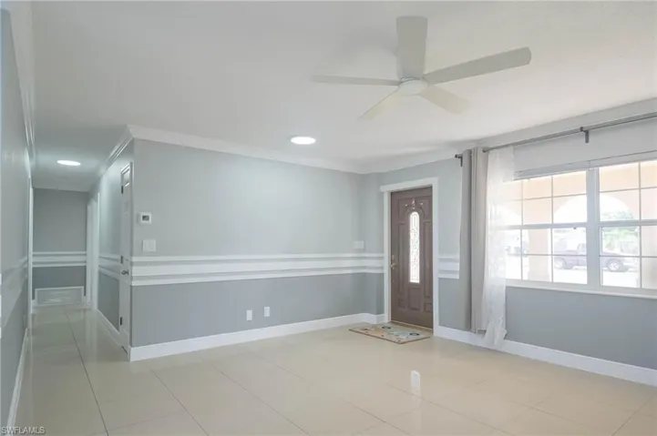 Entryway with light tile patterned flooring, ceiling fan, and ornamental molding