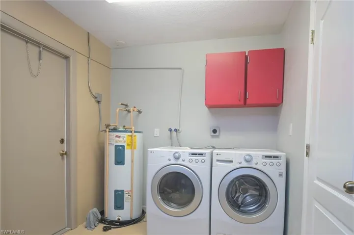 Laundry room featuring cabinets, water heater, washer and clothes dryer, and a textured ceiling