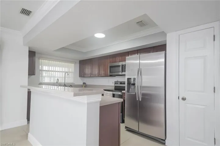 Kitchen featuring sink, ornamental molding, light tile patterned flooring, appliances with stainless steel finishes, and dark brown cabinets