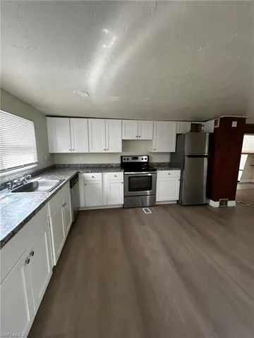 Kitchen with white cabinetry, dark hardwood / wood-style floors, stainless steel appliances, and sink