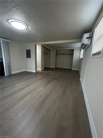 Basement featuring an AC wall unit, electric panel, and hardwood / wood-style flooring