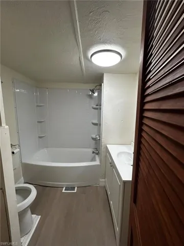 Full bathroom featuring vanity, washtub / shower combination, hardwood / wood-style flooring, and toilet