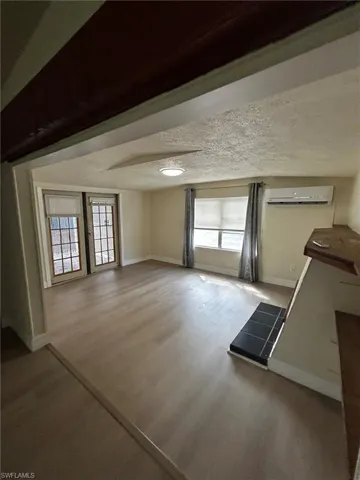 Unfurnished living room with a textured ceiling, a wall mounted AC, wood-type flooring, and plenty of natural light