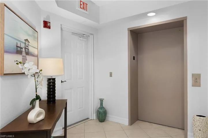 Corridor featuring elevator, light tile patterned floors, and baseboards