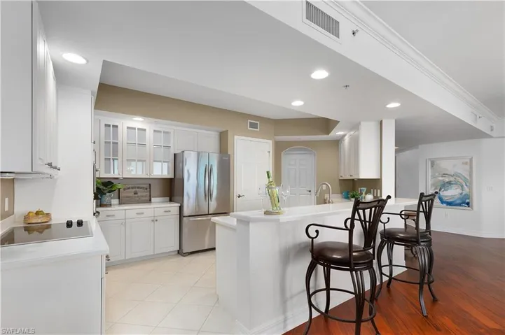 Kitchen featuring freestanding refrigerator, a peninsula, glass insert cabinets, recessed lighting, and white cabinetry