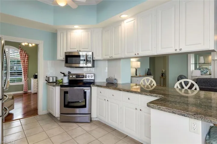 Kitchen with stainless steel appliances, dark stone counters, light tile patterned floors, white cabinets, and ceiling fan