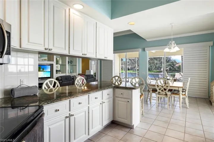 Kitchen with kitchen peninsula, white cabinets, hanging light fixtures, dark stone counters, and light tile patterned flooring