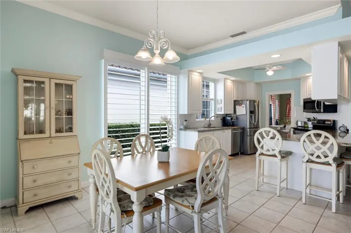 Dining area featuring crown molding, light tile patterned flooring, sink, and ceiling fan with notable chandelier