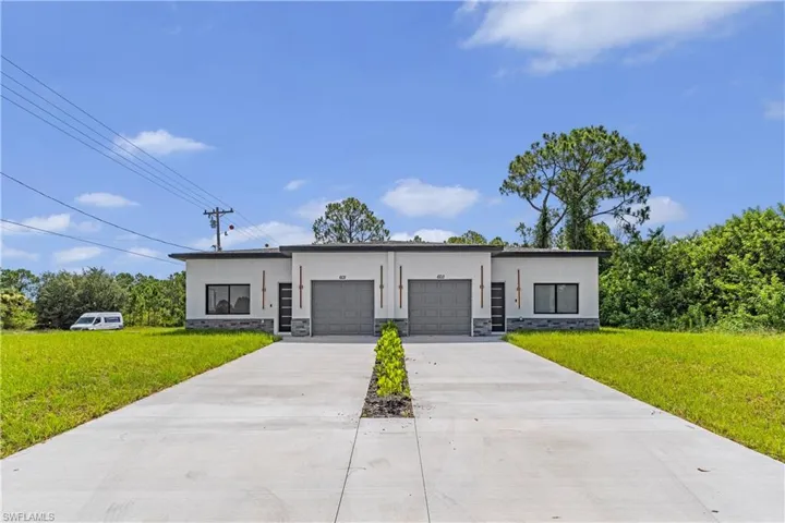 Modern duplex property featuring a clean stucco exterior, stone veneer accents, individual garage doors, contemporary entrance doors with vertical glass inserts, and a shared concrete driveway