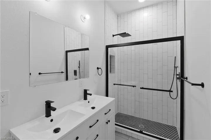 Modern bathroom featuring a dual-sink vanity with matte black fixtures, a contemporary walk-in shower with subway tile surround, a built-in shower niche, a rain shower head, and a handheld shower unit