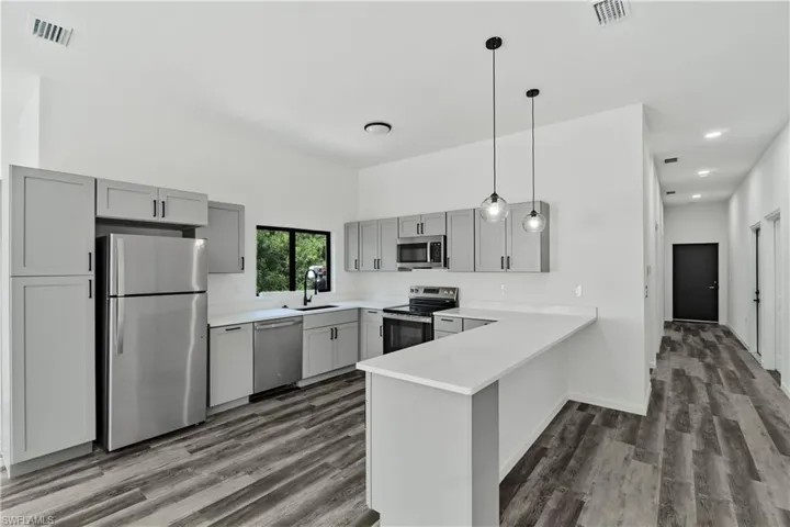 Open-concept kitchen featuring gray shaker cabinetry, stainless steel appliances, white countertops, and wood-finish flooring