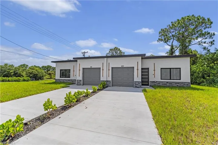 Modern duplex featuring stucco exterior with stone accents, individual single-car garages, contemporary entry doors, and expansive concrete driveways