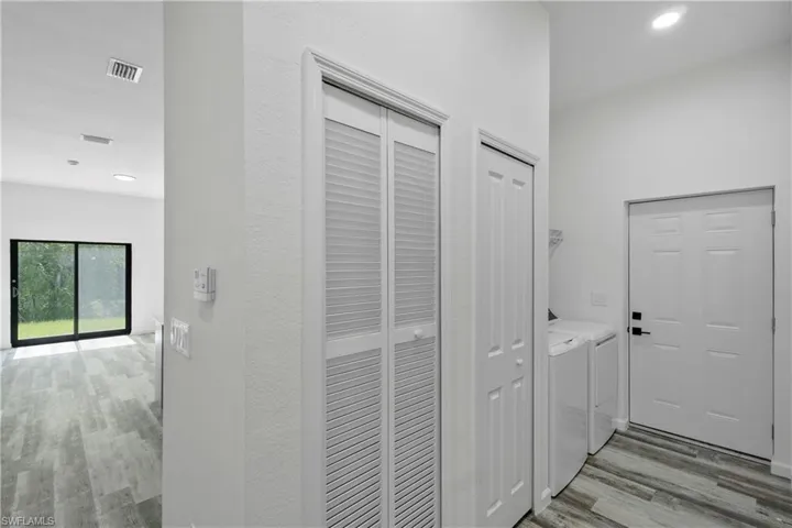 Utility area featuring wood-finish flooring, a louvered bi-fold closet, a six-panel door, and recessed lighting