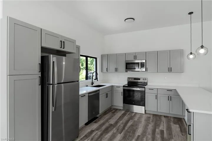 Contemporary kitchen featuring light gray shaker cabinetry with matte black hardware, white countertops, and wood-finish flooring