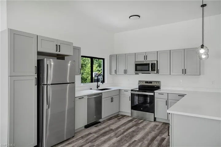 Modern kitchen featuring light gray cabinetry with black hardware, stainless steel appliances, white countertops, and wood-finish flooring