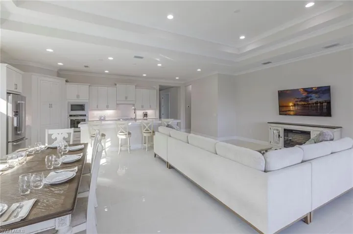 Living room with a tray ceiling, sink, light tile patterned floors, and ornamental molding