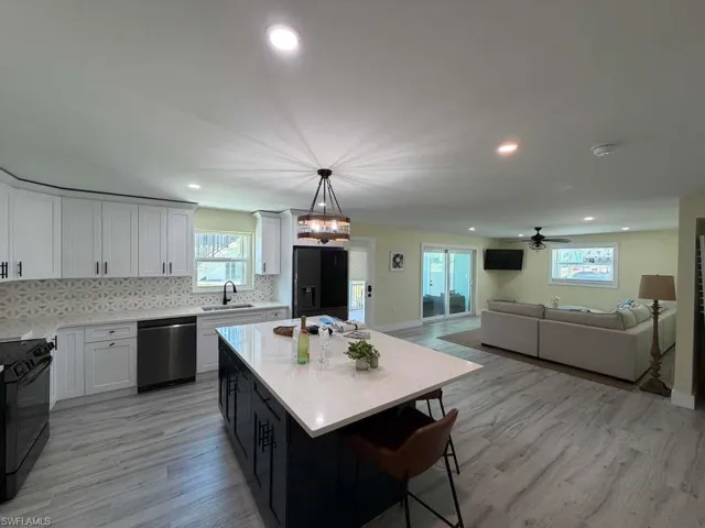 Contemporary kitchen featuring white cabinetry, a patterned tile backsplash, stainless steel appliances, and a dark island with a light-colored countertop