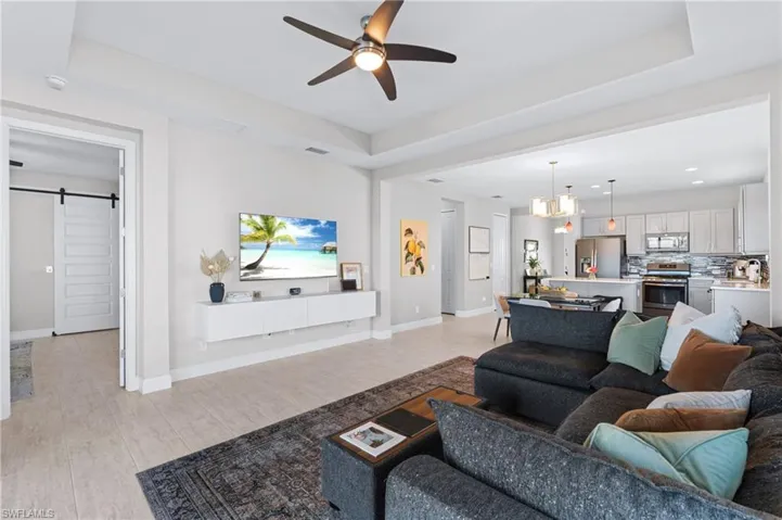 Living room with a barn door, a raised ceiling, ceiling fan with notable chandelier, and light hardwood / wood-style flooring