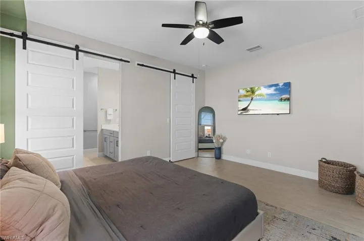 Bedroom with light hardwood / wood-style floors, a barn door, ceiling fan, and ensuite bathroom