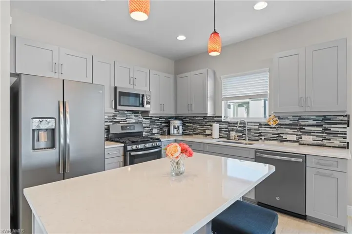 Kitchen featuring sink, tasteful backsplash, decorative light fixtures, appliances with stainless steel finishes, and a kitchen island